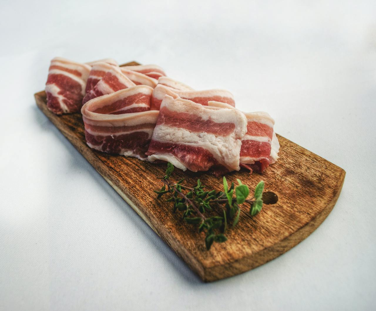 Sliced bacon laid on a rustic wooden board with herbs, showcasing a delicious and inviting food presentation.