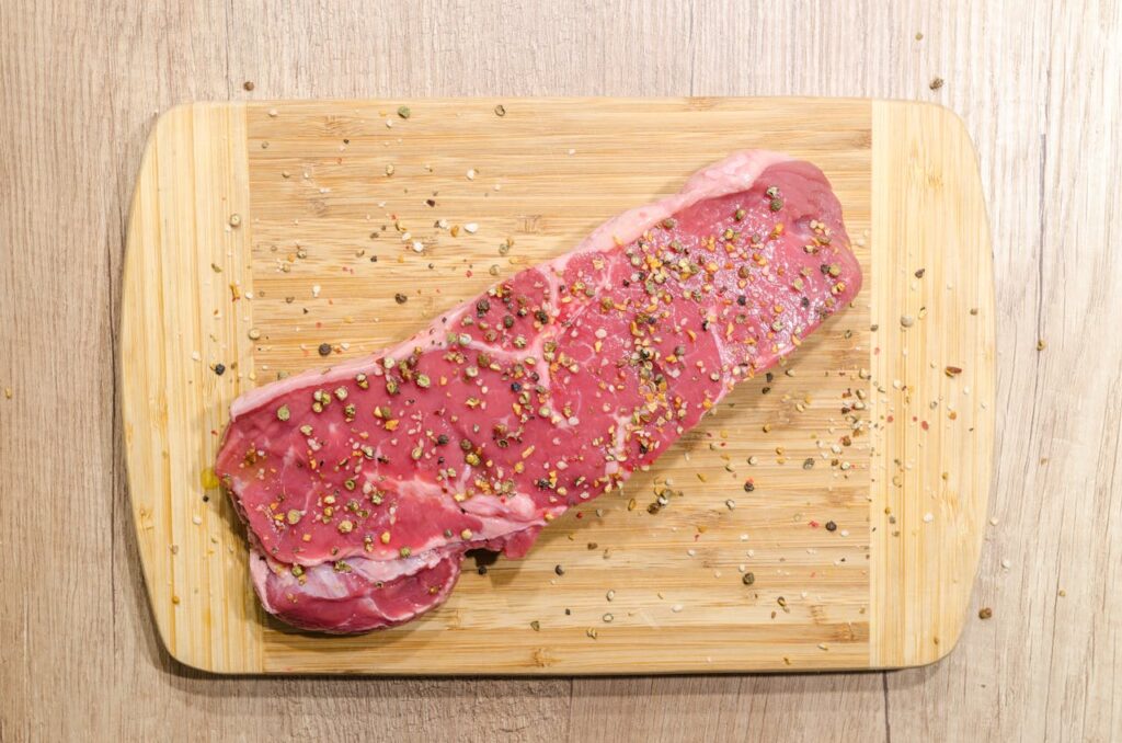 Raw beef steak seasoned with spices on a wooden chopping board. Perfect for cooking enthusiasts.