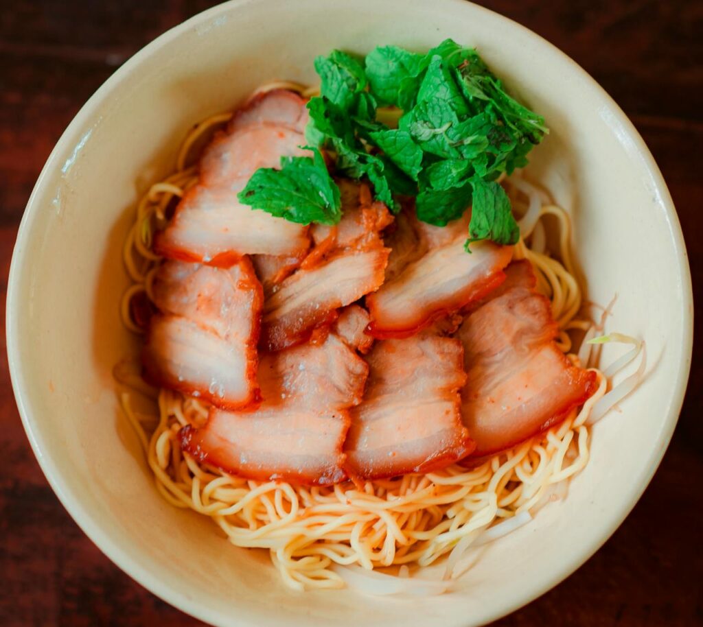 Appetizing bowl of pork noodles garnished with fresh greens, captured from above.